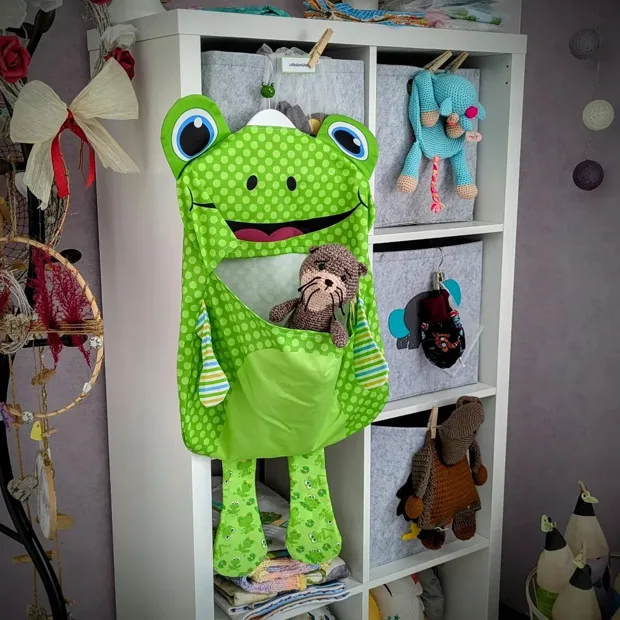 Grüner gehäkelter Frosch vor einem weißen Regal